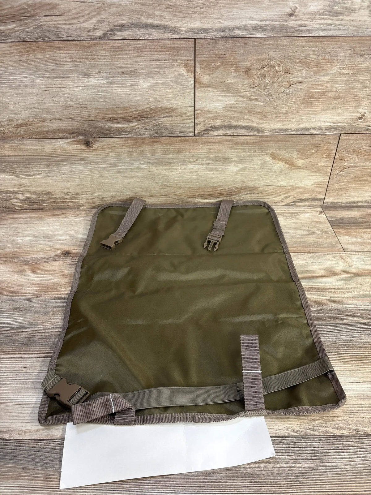 Top-down view of Tike Smart Clean-Edge kick mat showing olive-green waterproof surface and adjustable straps on wood floor