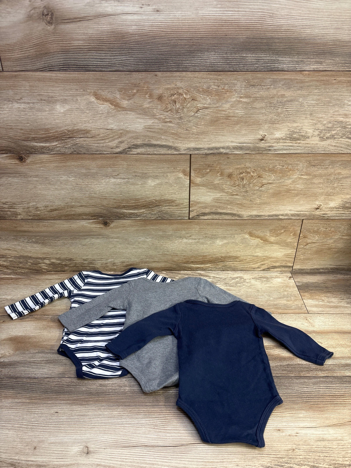 Top view of Hudson Baby 3-pack long-sleeve bodysuits in navy, gray, and navy-and-white stripes on a wood background