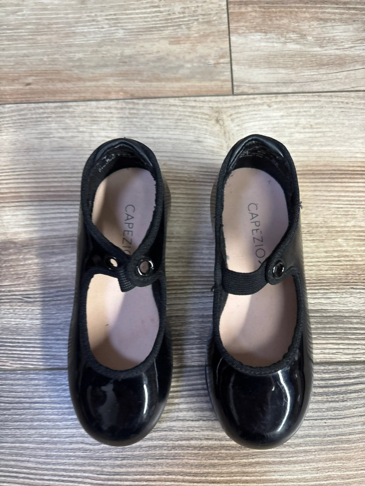 Black Capezio children's tap shoes with elastic straps on wood floor