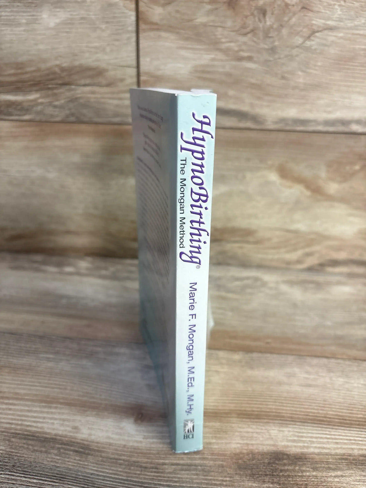 Side view of HypnoBirthing paperback book showcasing the spine title and author on a wood background