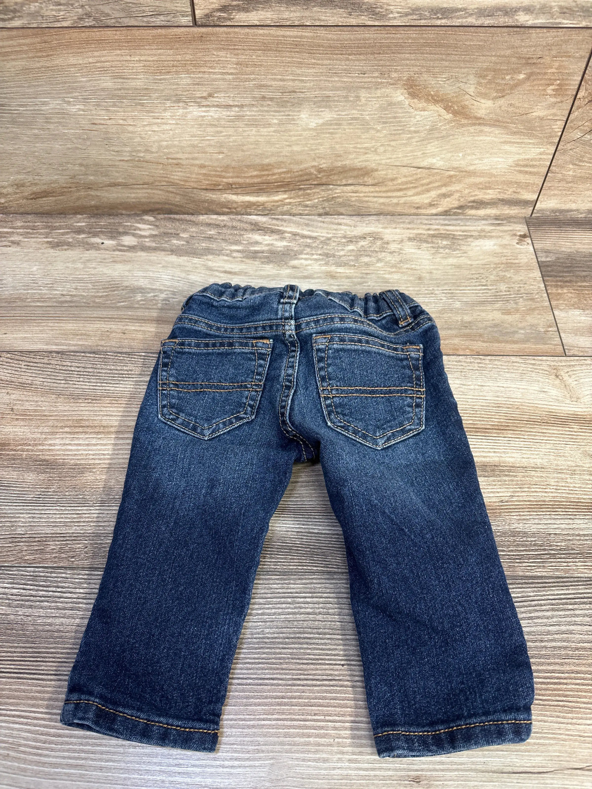 Back view of Oshkosh Classic blue denim jeans for infants size 6m on a wooden background.