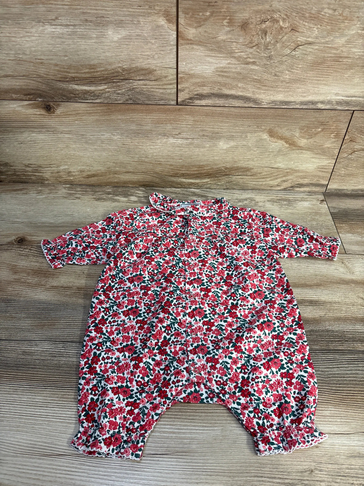 Front view of Petite Plume red twill floral romper showcasing long sleeves and ruffled trim on a wood floor