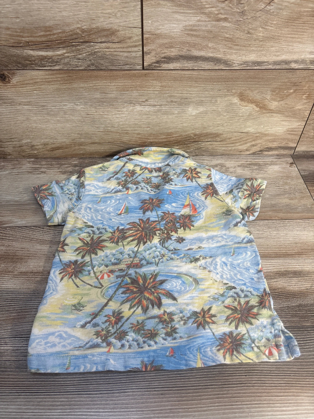 Back view of Polo Ralph Lauren light blue tropical polo jersey size 3T showing palm tree and sailboat print on wood background