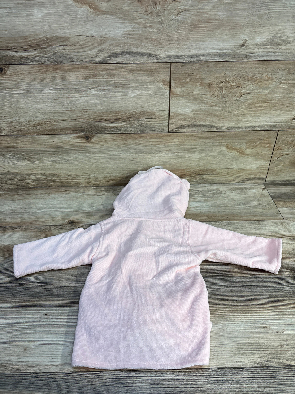 Back view of pink Le Petit Elephant hooded baby bathrobe (0–12 months) showing hood with small ear details on wood surface