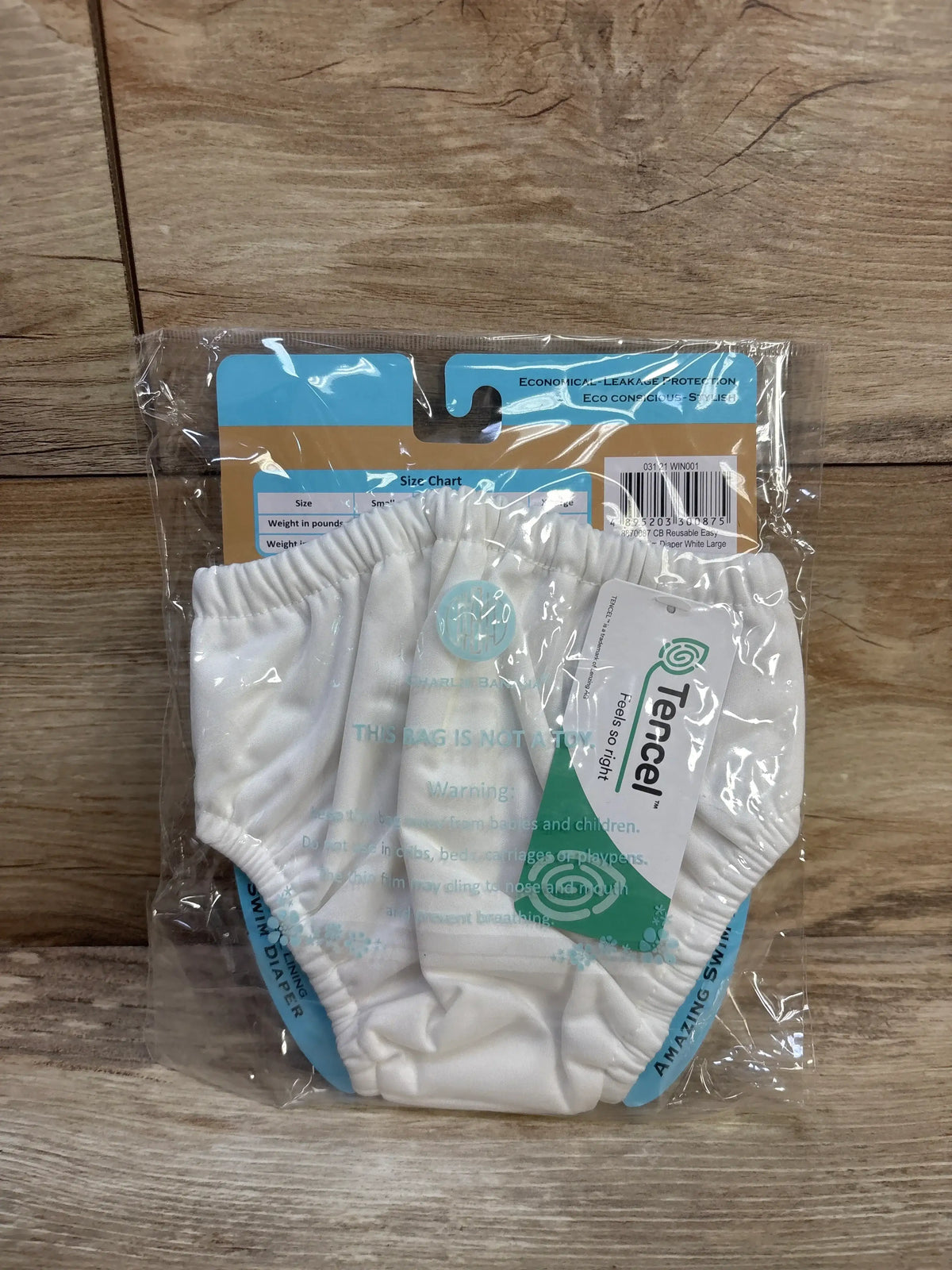 Front view of Charlie Banana white reusable swim diaper, size Large (18-36 mo), elastic waistband and leg openings in clear plastic packaging on wood