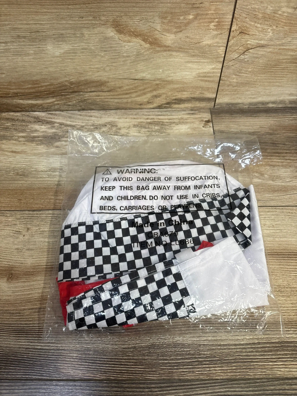 Top-down view of toddler chef costume in clear bag showing white chef hat, checkered apron and red neckerchief on wooden floor
