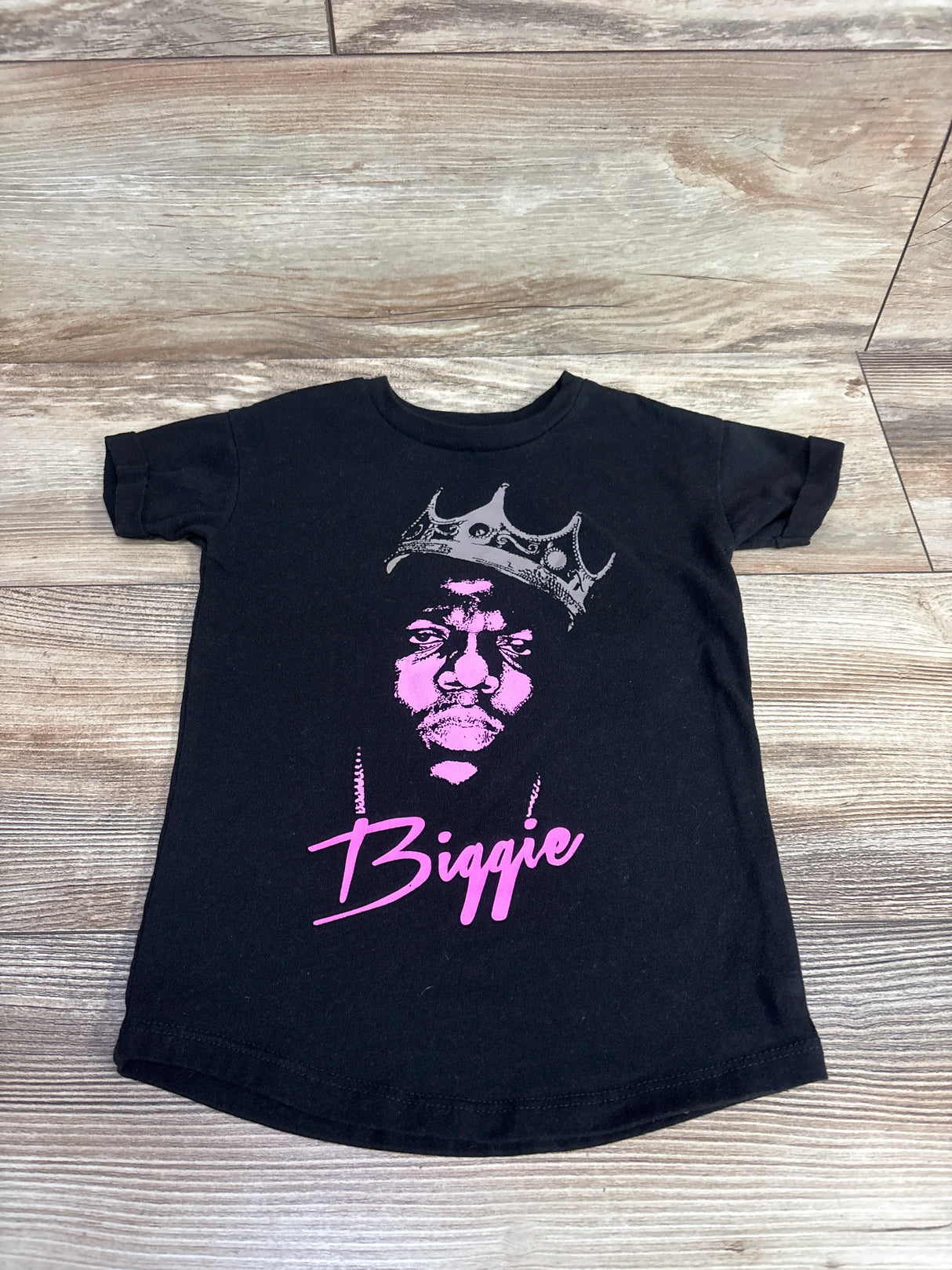 Black kids t-shirt with pink graphic of rapper Biggie wearing a crown on wooden floor