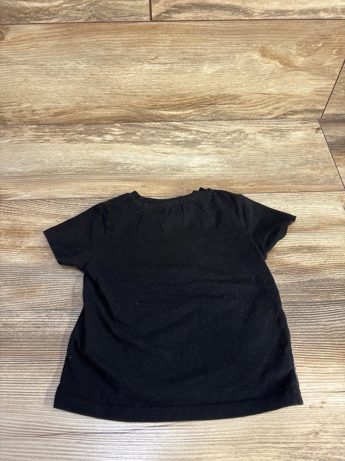 Back view of a black Guess Kids short sleeve shirt for toddlers, size 2T, on a wood floor.