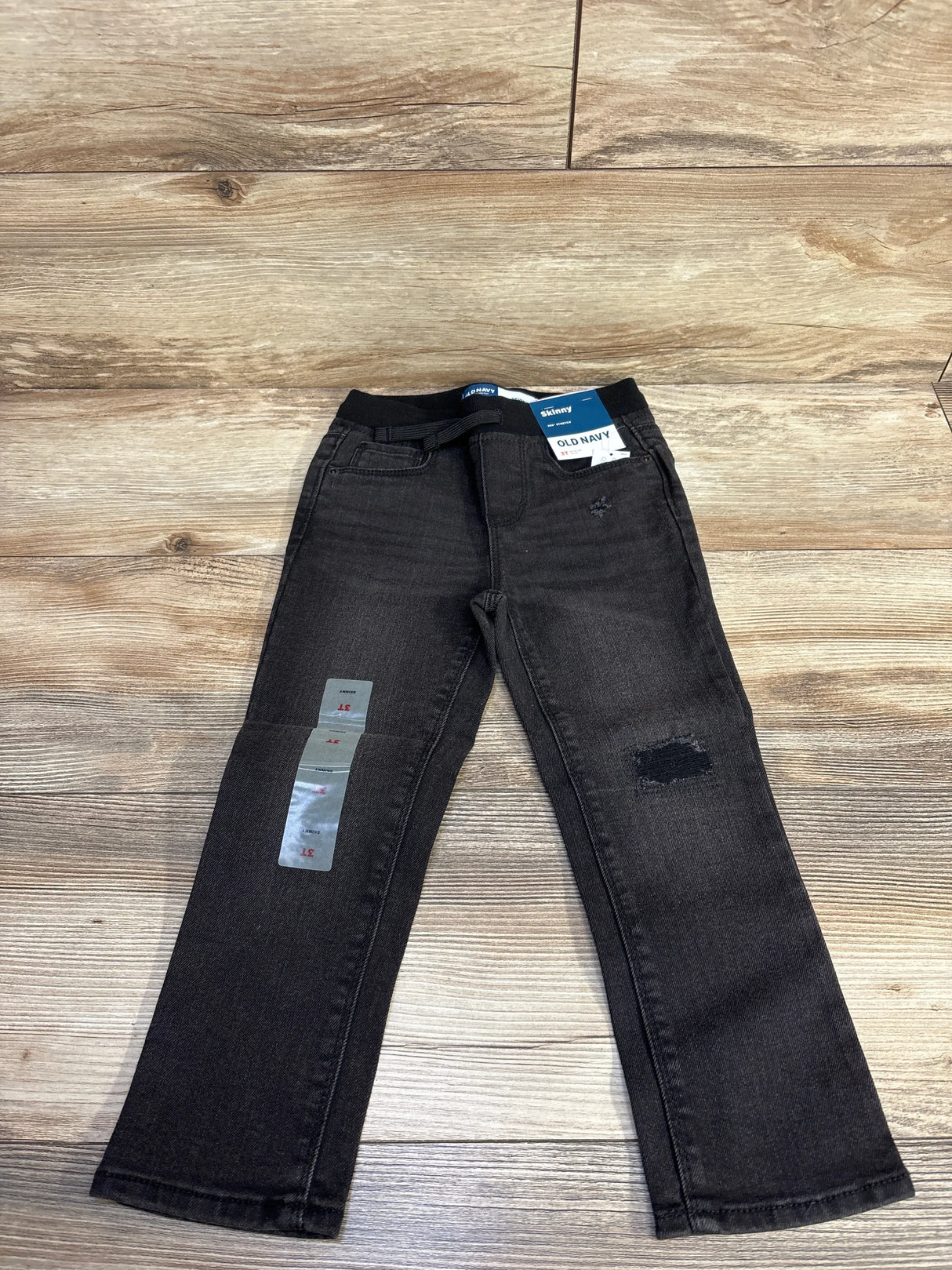 Black Old Navy kids skinny jeans with distressed patch and adjustable waistband on wooden floor