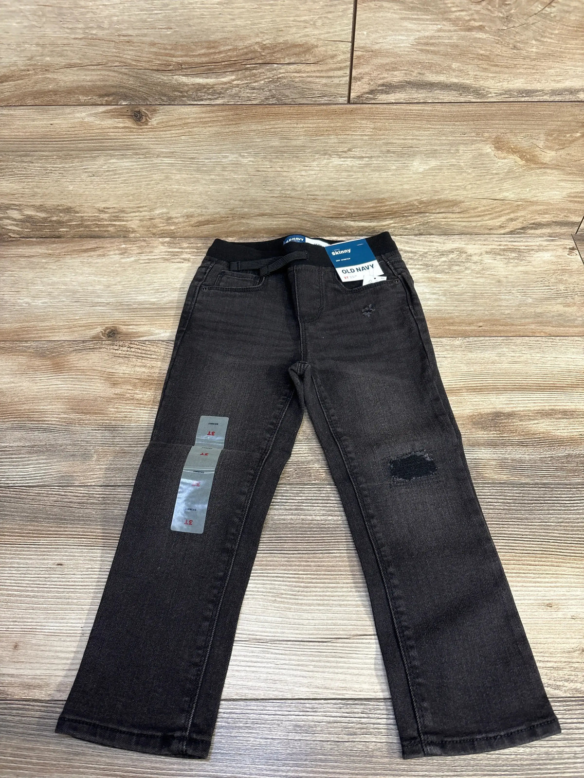 Black Old Navy kids skinny jeans with distressed patch and adjustable waistband on wooden floor