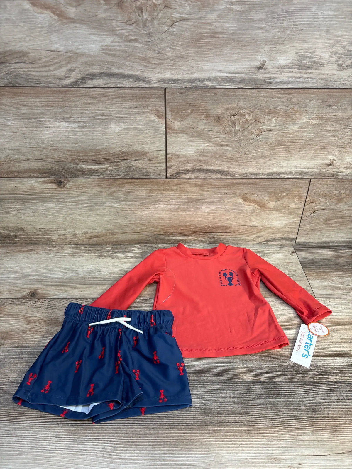 Long sleeve red toddler swim shirt and blue lobster print swim trunks on wood floor