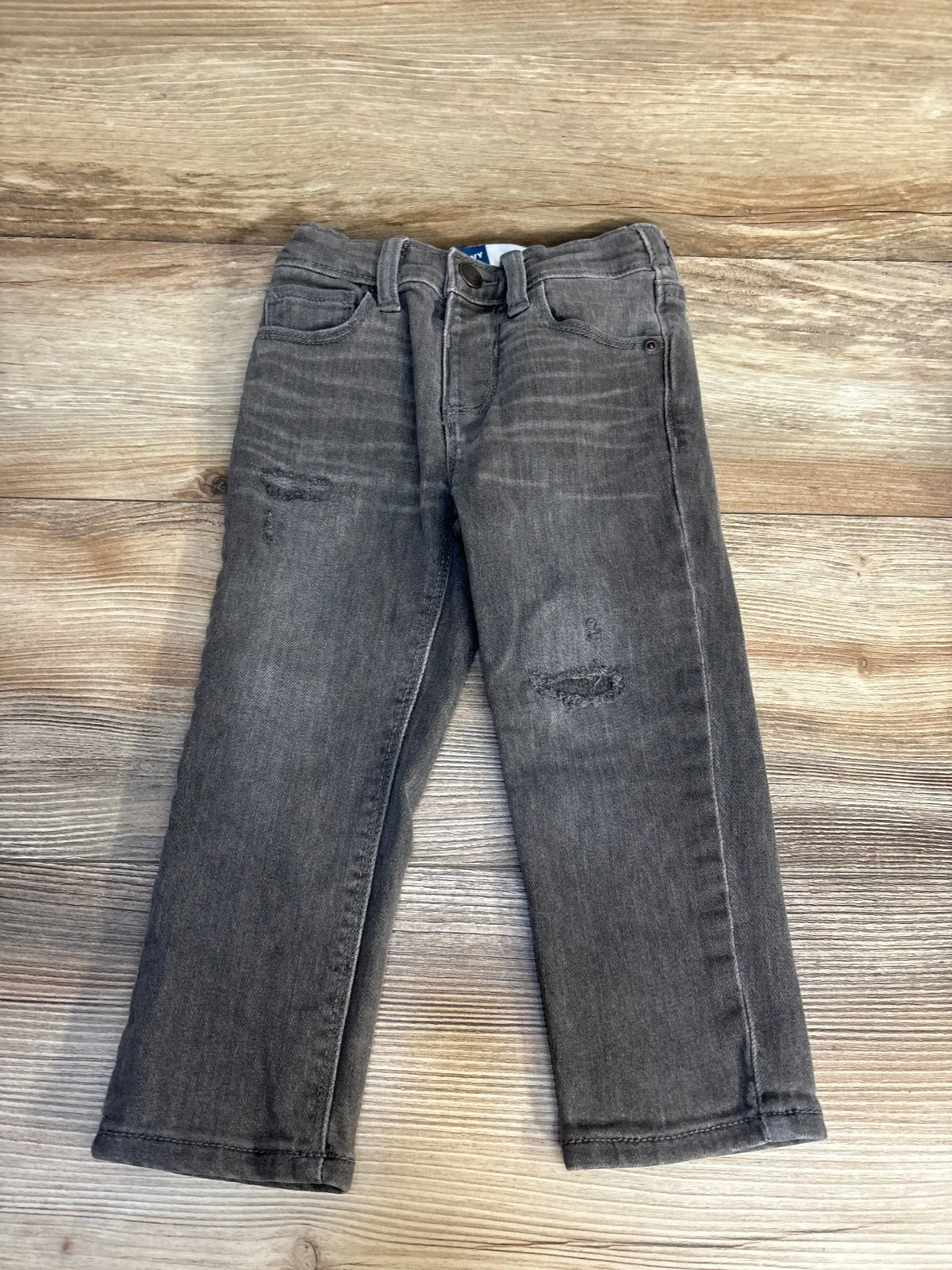 Top-down view of grey 2T Old Navy distressed jeans showing ripped knees and front pockets on wood background
