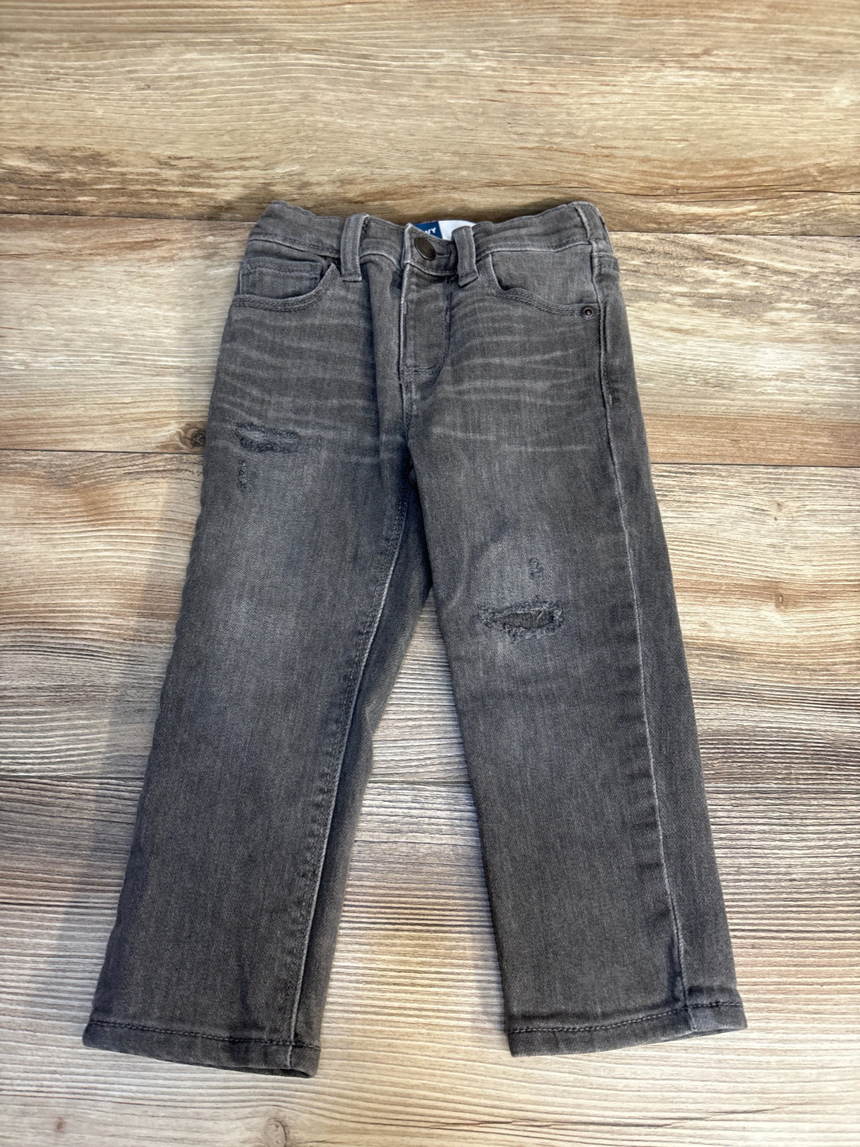 Top-down view of grey 2T Old Navy distressed jeans showing ripped knees and front pockets on wood background