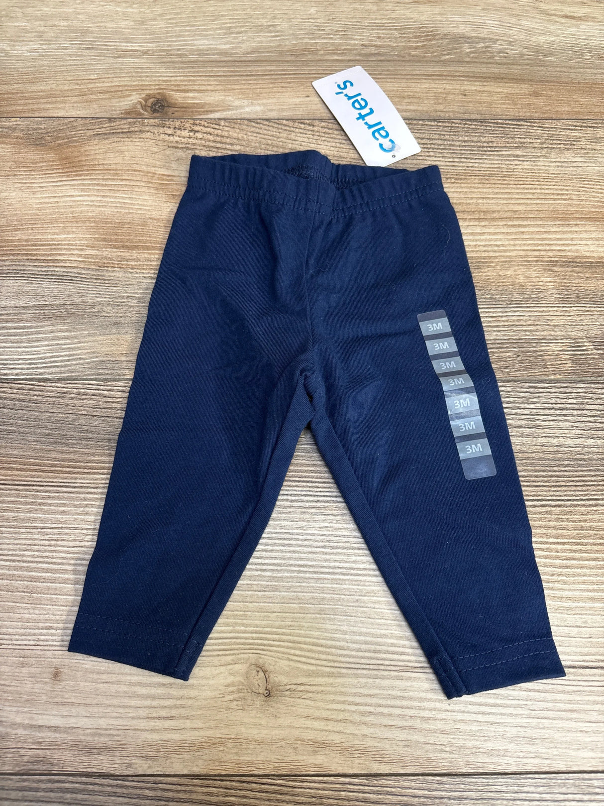 Flat lay of Carter’s navy cotton stretch baby leggings showing elastic waistband and 3M size stickers on a wood background