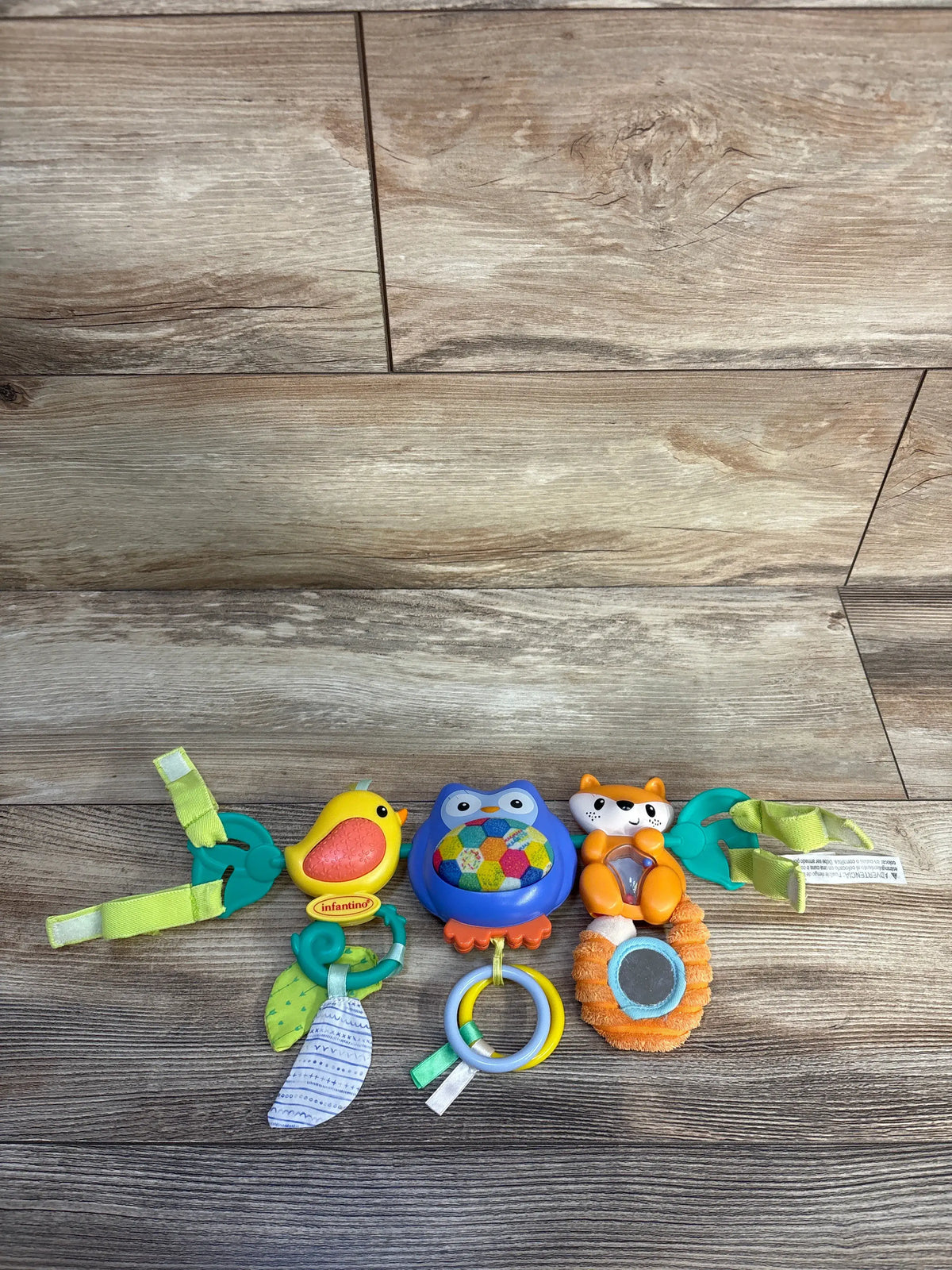 Overhead view of Infantino Go gaga! Musical Travel Bar Activity Toy with owl, bird, cat, mirror, and straps on wood floor
