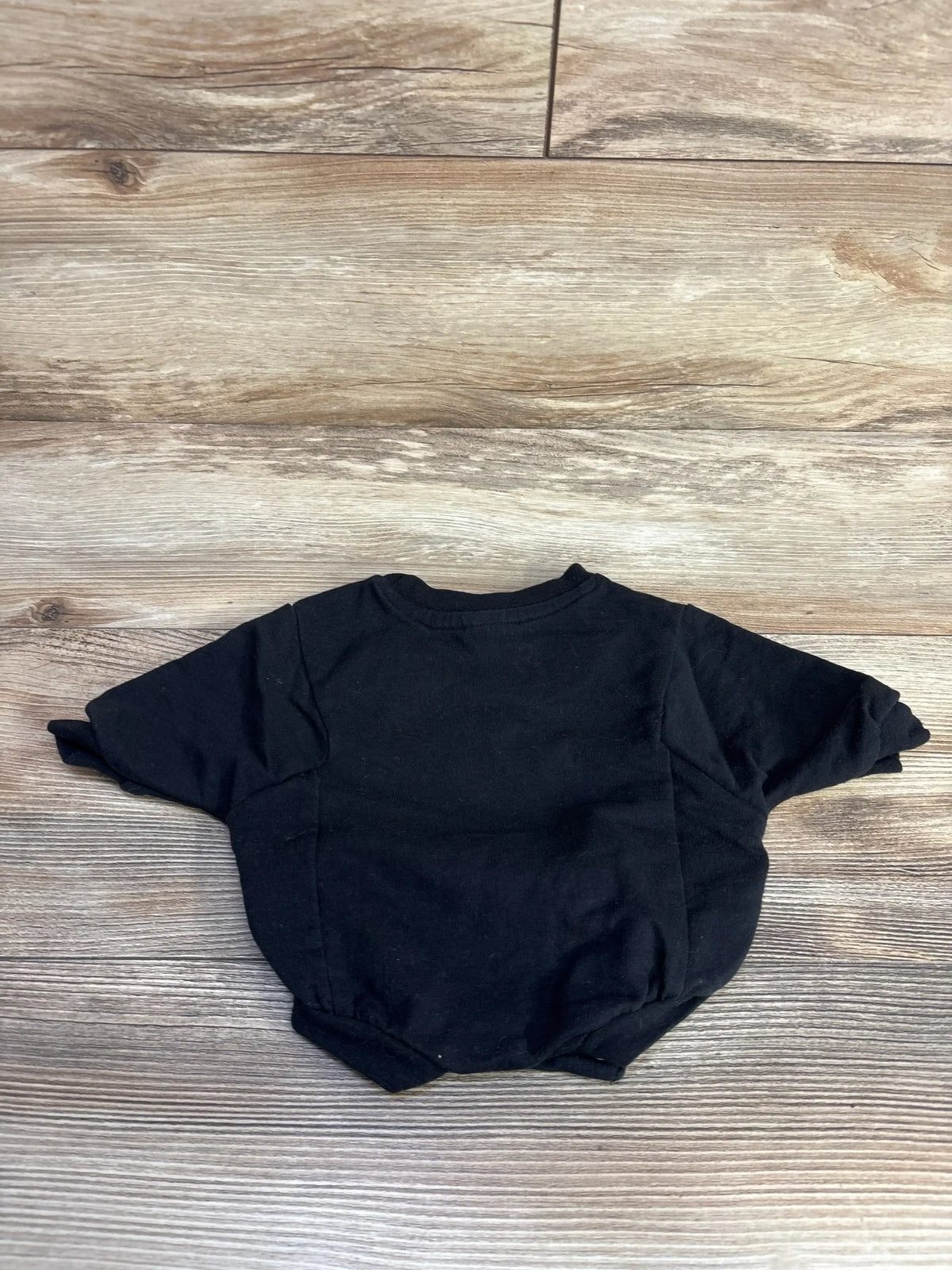 Back view of Cat and Jack newborn black bat romper showing short sleeves and elasticized leg openings on wood background
