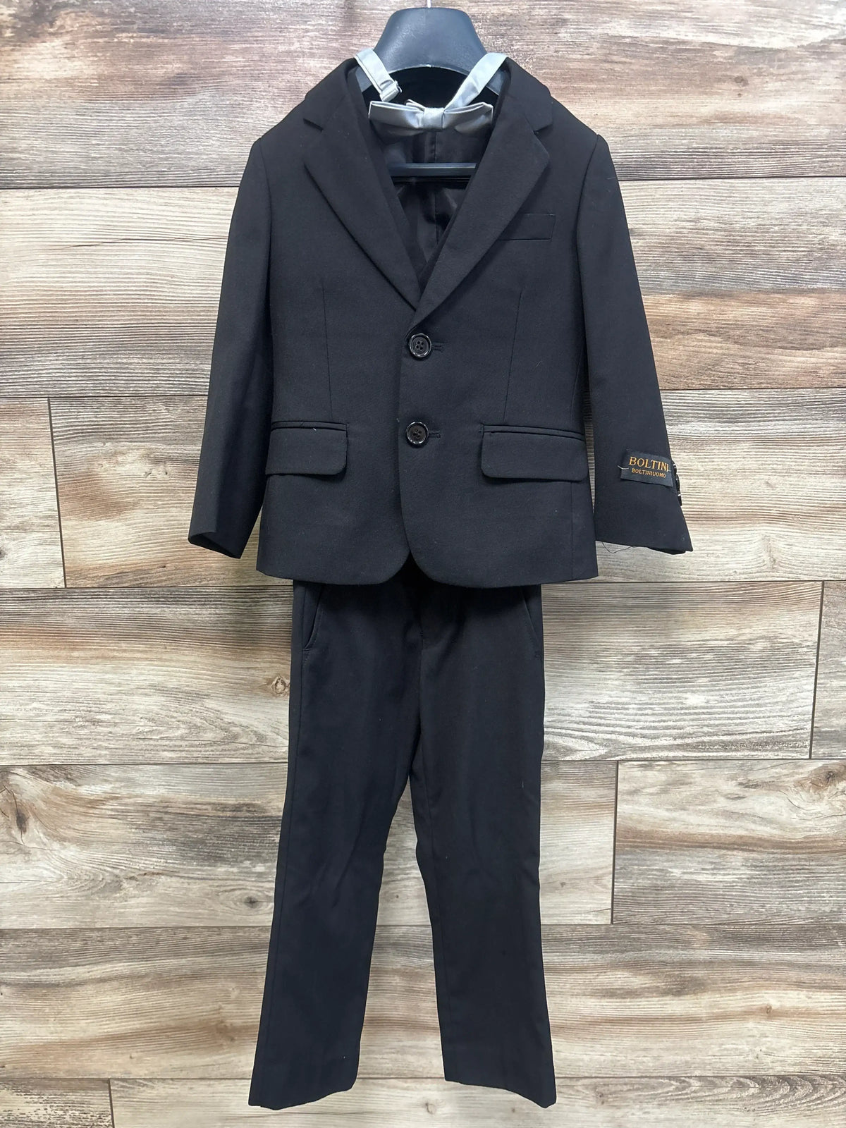 Front view of Boltini black 4-piece suit set showcasing notch lapel blazer, vest, dress pants, and bowtie on wood flooring