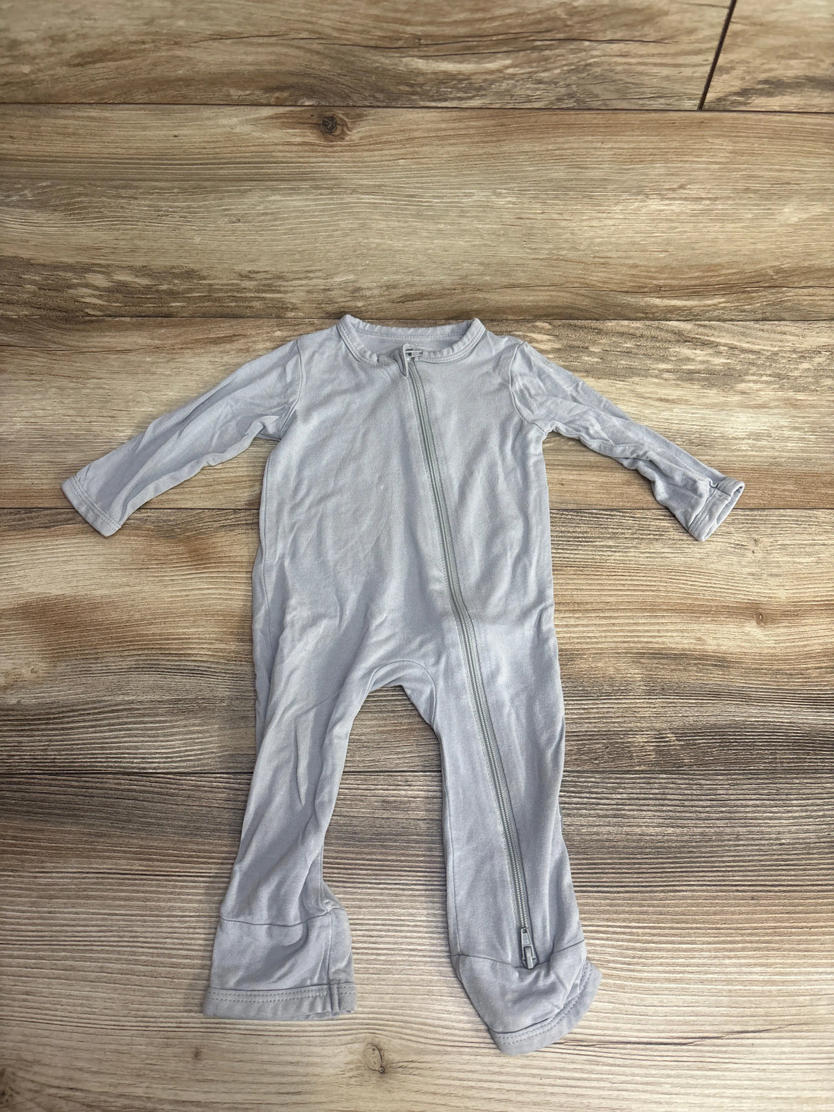 Light gray long-sleeve baby footed sleeper with diagonal zipper on wooden floor