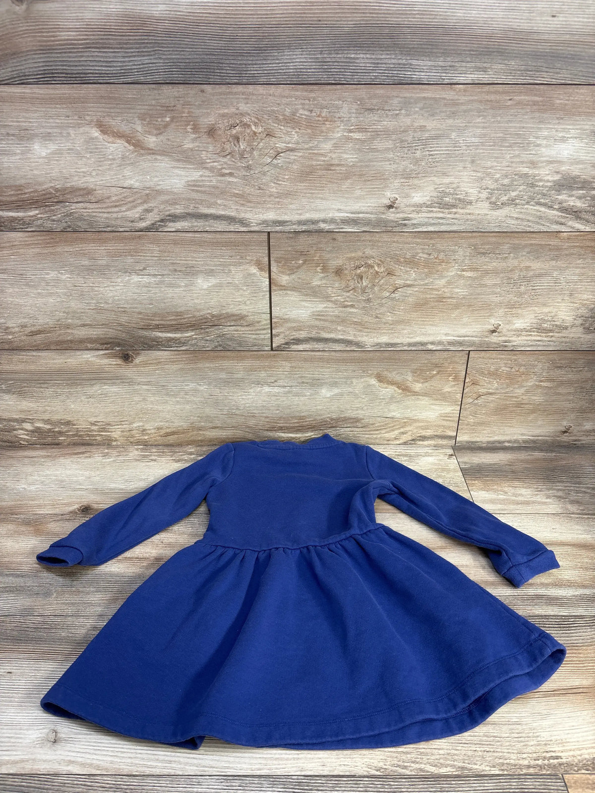 Top-down view of a Mini Boden navy embroidered sweatshirt dress showcasing long sleeves and a gathered skirt on a wood-look background