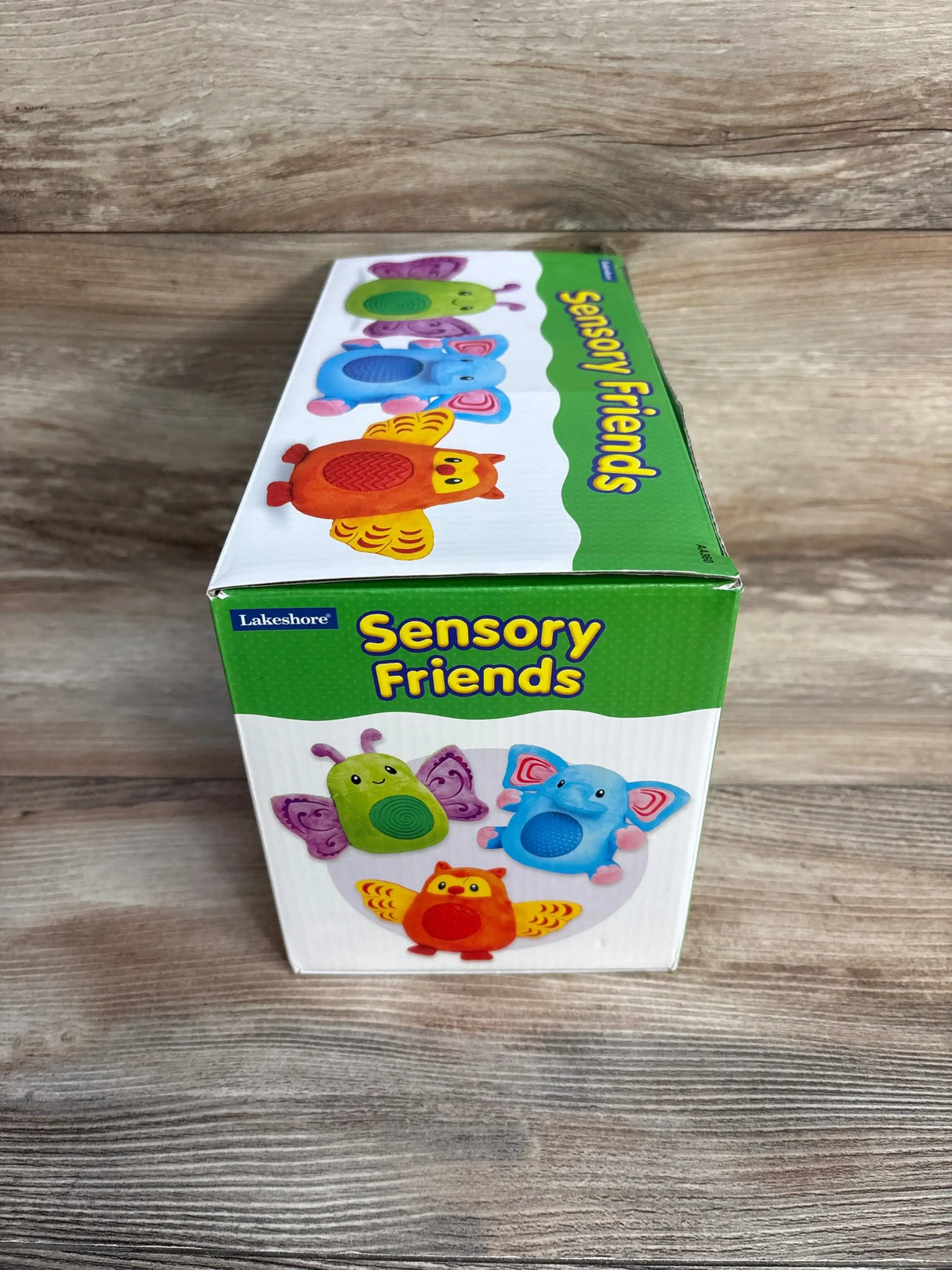 Angled top-front view of Lakeshore Sensory Friends box showcasing artwork of three colorful textured toy animals with a wood tabletop background