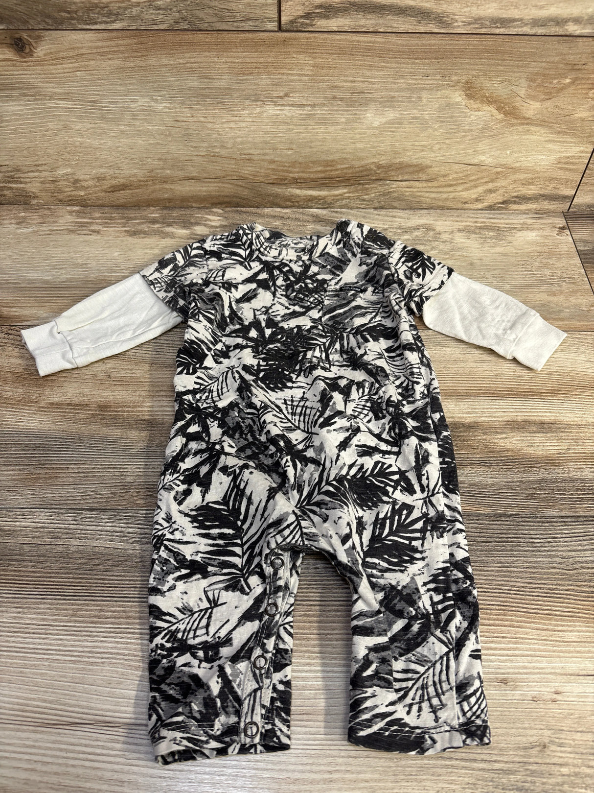 Black and white tropical leaf baby romper with long sleeves on wood background