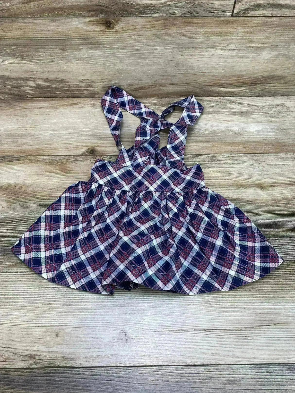 Flat lay of suspender plaid skirt showcasing crisscross straps and gathered skirt with wood floor background size 18M
