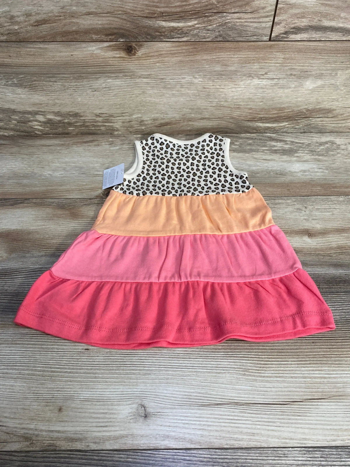 Flat lay of baby tank tiered dress showcasing leopard-print bodice and peach and coral tiered skirt on wood background
