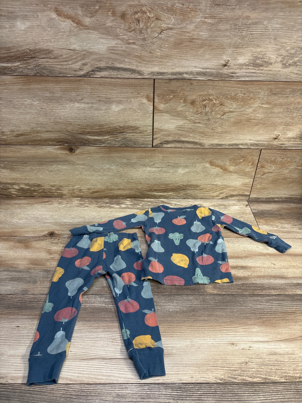 Flat lay of Little Planet Organic blue 2-piece pajamas long-sleeve top and cuffed pants with multicolor fruit print on wood