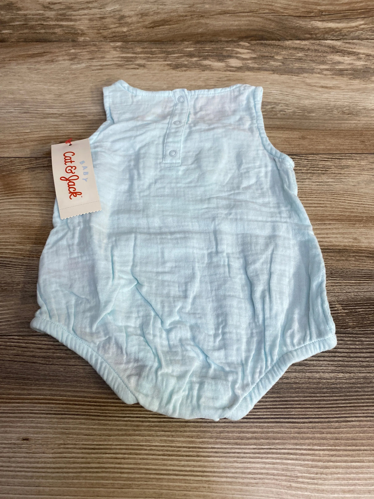 Flat-lay of Cat & Jack gauze bunny romper showcasing back neck snap closure and elastic leg openings on wood background