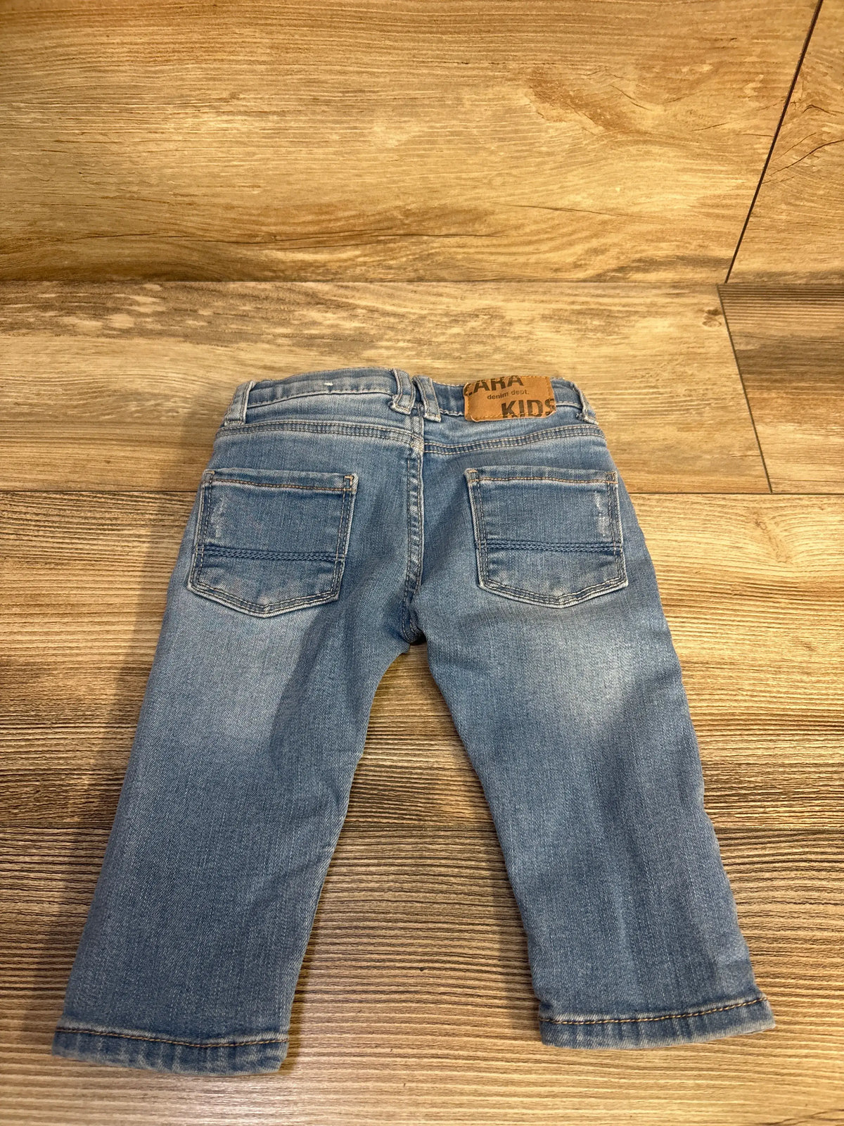 Rear view of Zara denim jeans in blue, size 3–6 months, showcasing two back pockets on a wood floor