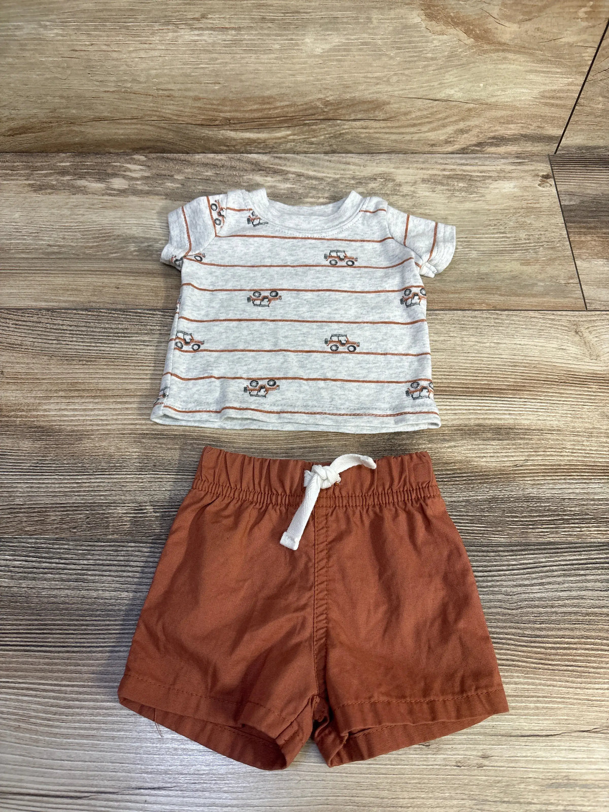Top view of Just One You newborn shirt and shorts set showcasing vehicle-print shirt and drawstring shorts on a wood floor