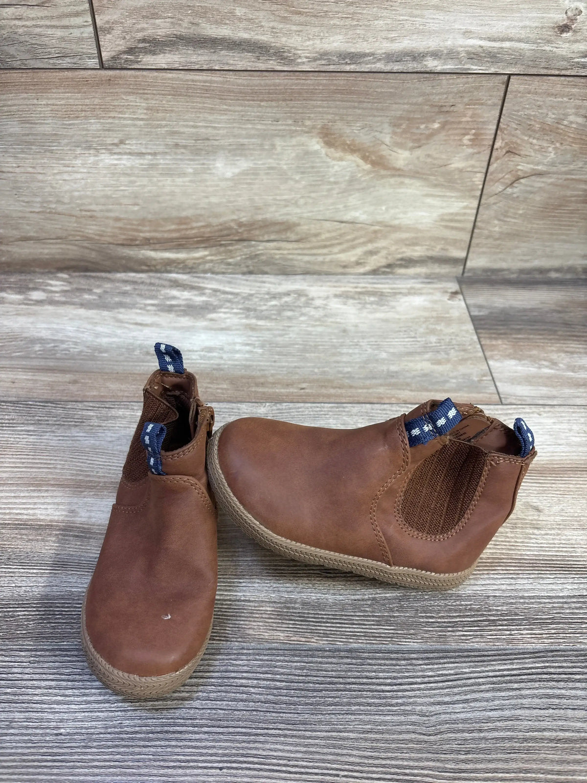Front view of Cat & Jack brown toddler zipper ankle boots showing elastic side panel and blue pull tabs on wood floor