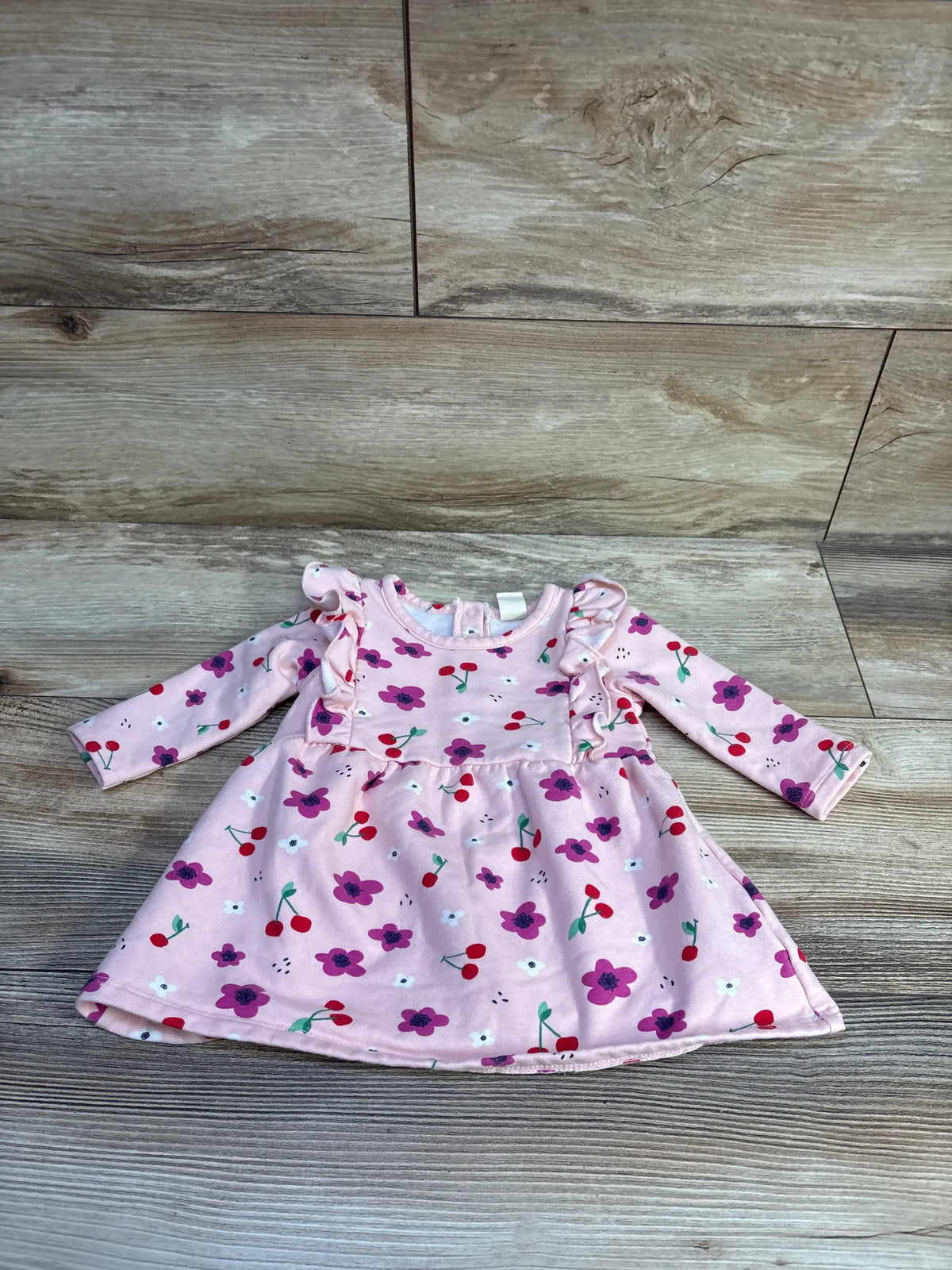 Front view of pink cherry print sweatshirt dress showcasing ruffled shoulders and flared skirt on a wood-look floor