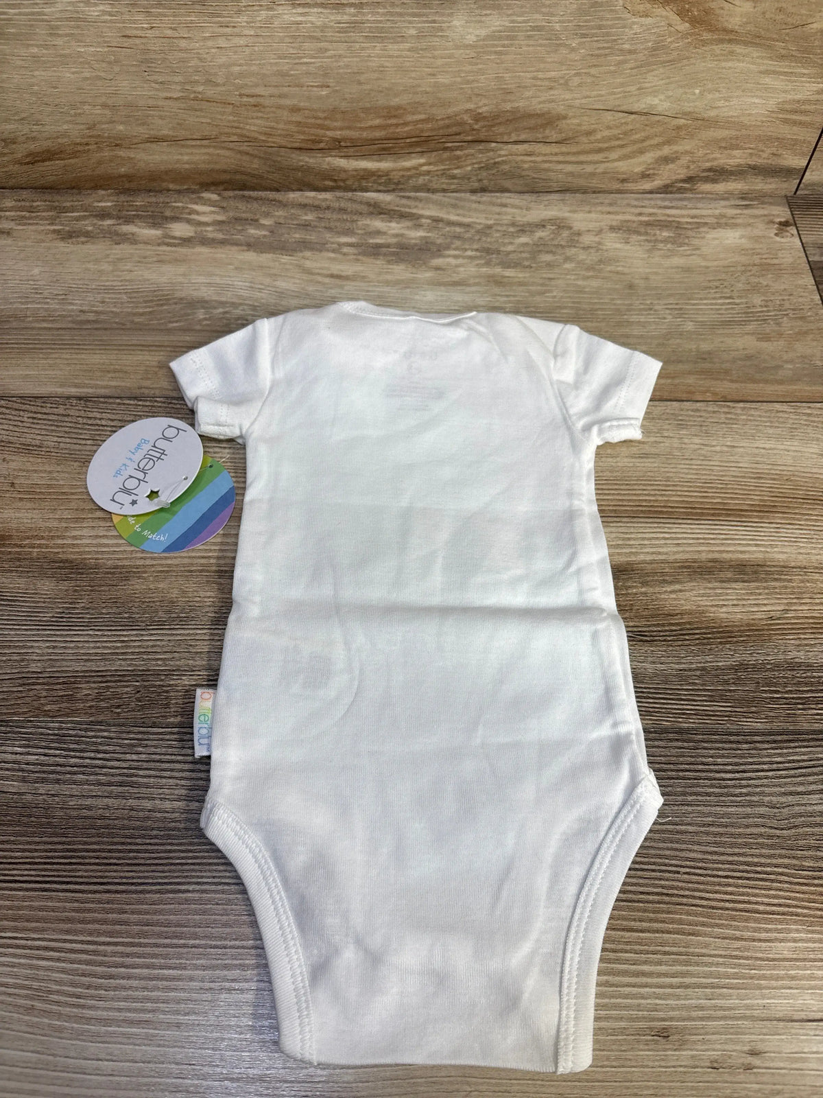 Flat lay of white Butterblu organic cotton bodysuit showcasing short sleeves and leg openings on a wood-grain background