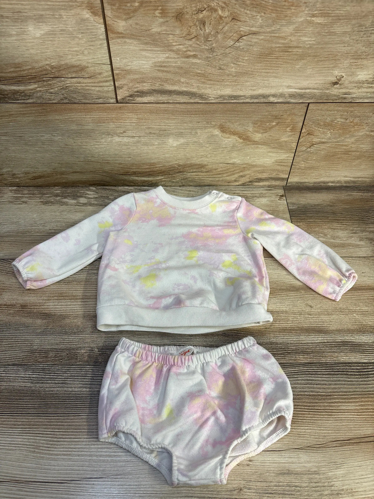 Front view of Cat and Jack tie-dye sweatshirt and bloomers set in size 12 months with pink and yellow pattern on wood floor