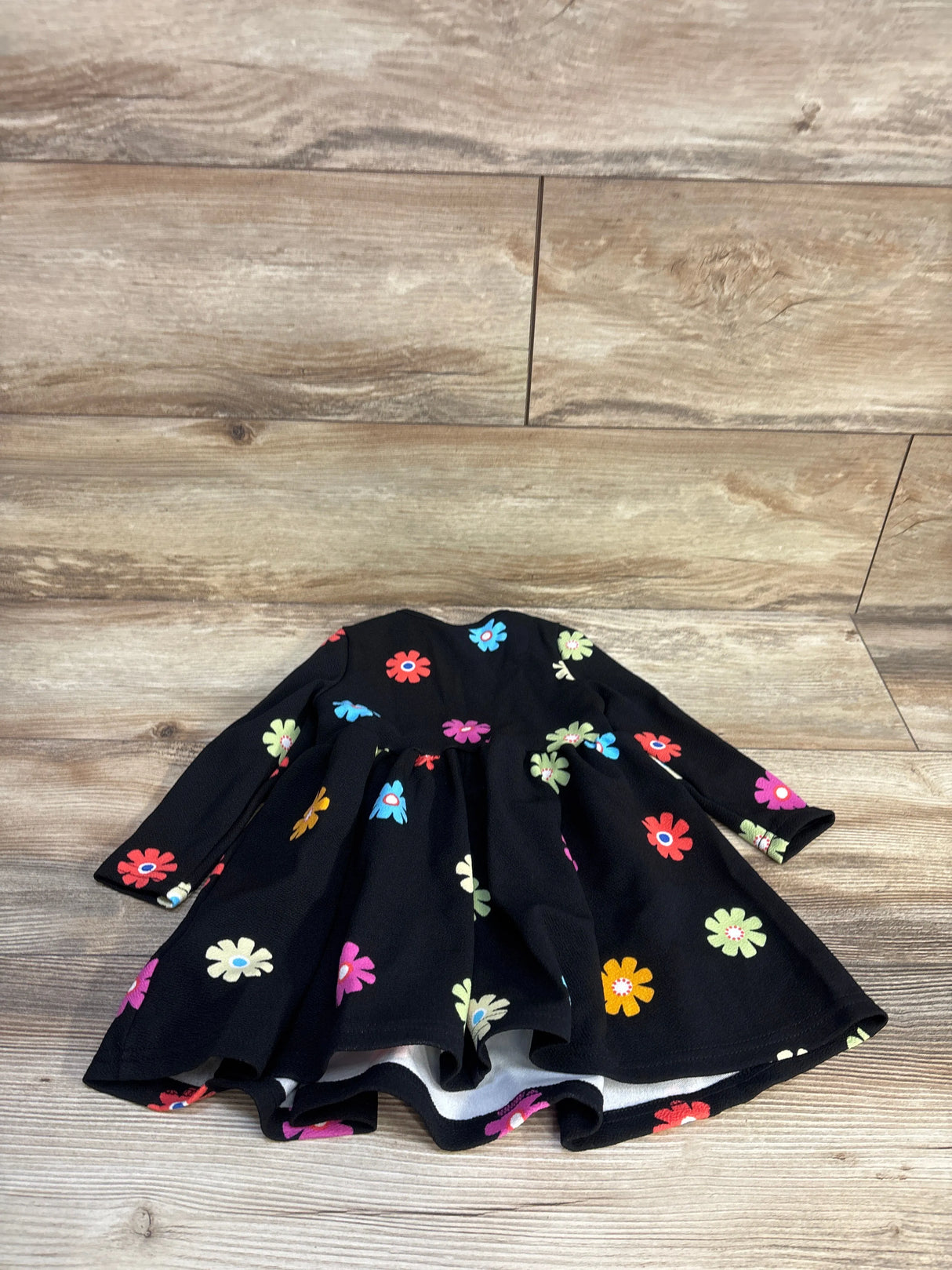 Top-down view of toddler black long-sleeve floral dress showcasing colorful daisy print and gathered skirt on wood floor