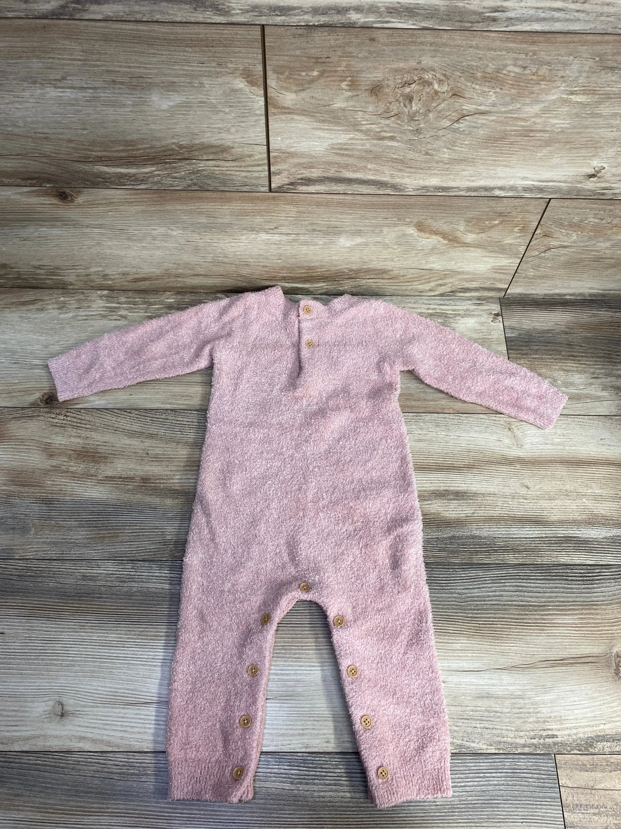Soft pink fuzzy baby onesie with long sleeves and wooden buttons on gray wood floor