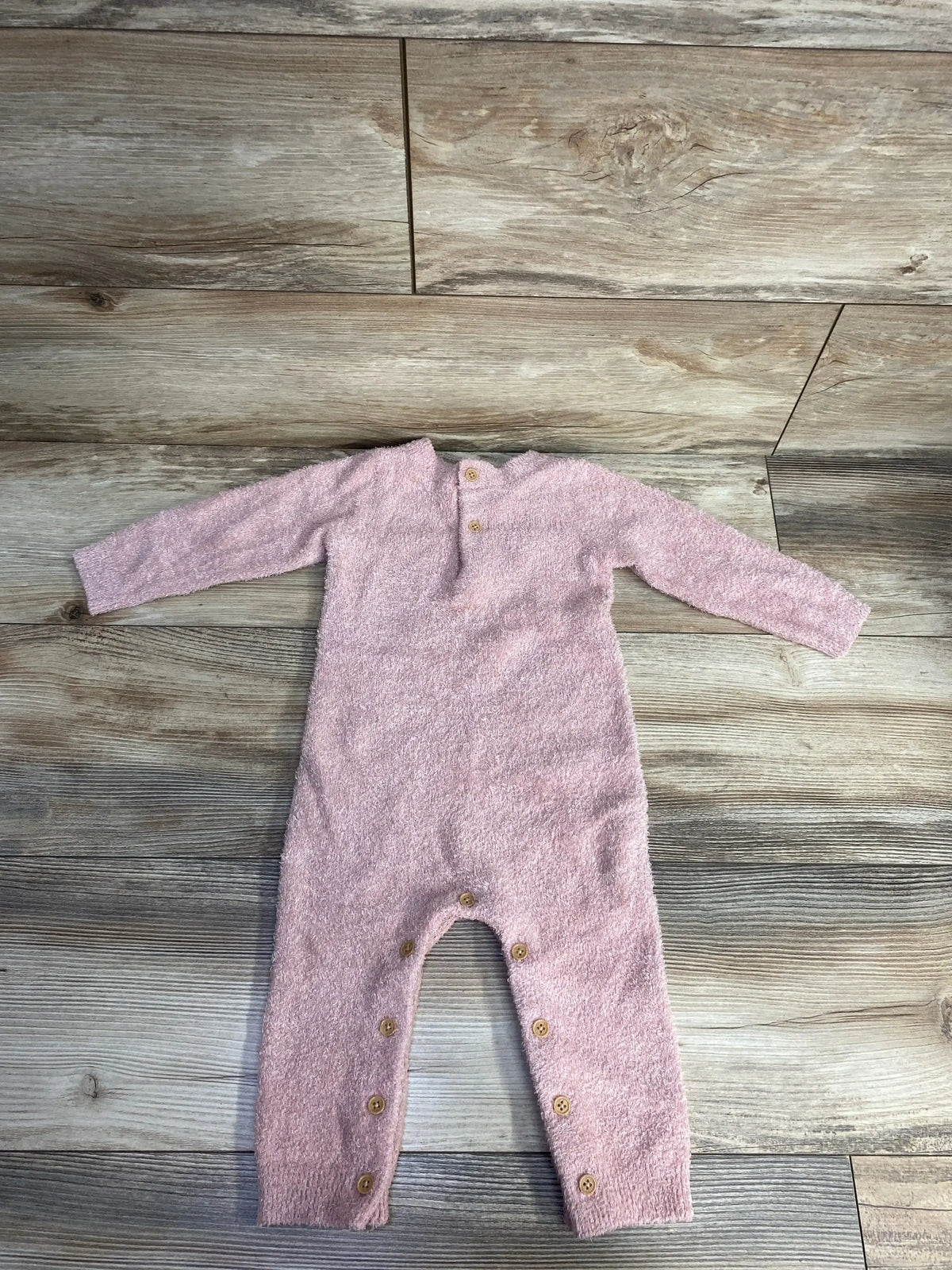 Soft pink fuzzy baby onesie with long sleeves and wooden buttons on gray wood floor