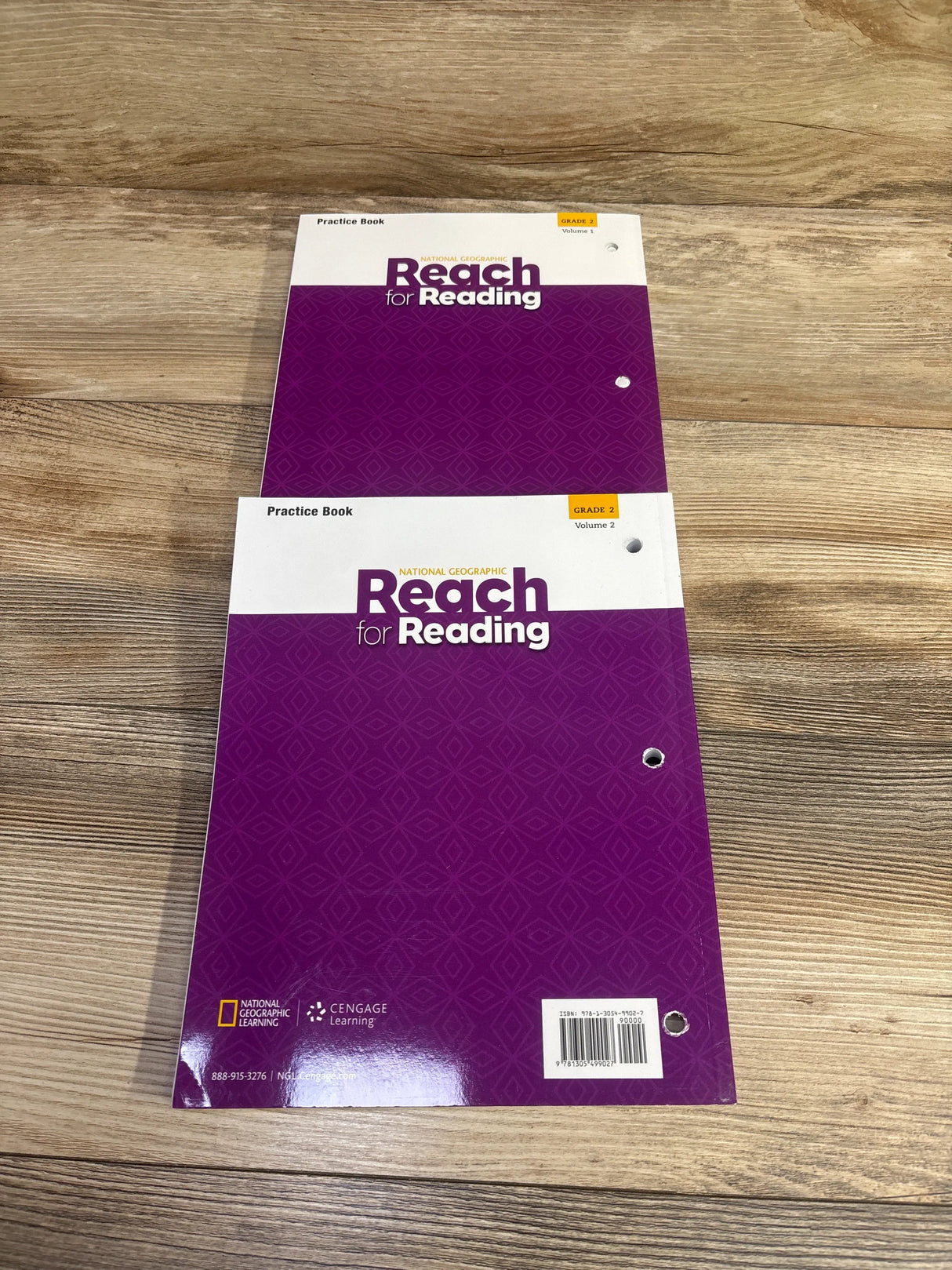 Two National Geographic Reach for Reading Grade 2 practice books on wood surface