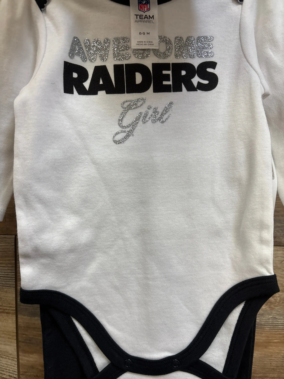Front view of white Raiders bodysuit with black footed pants showing glitter Awesome Raiders Girl text and snap crotch