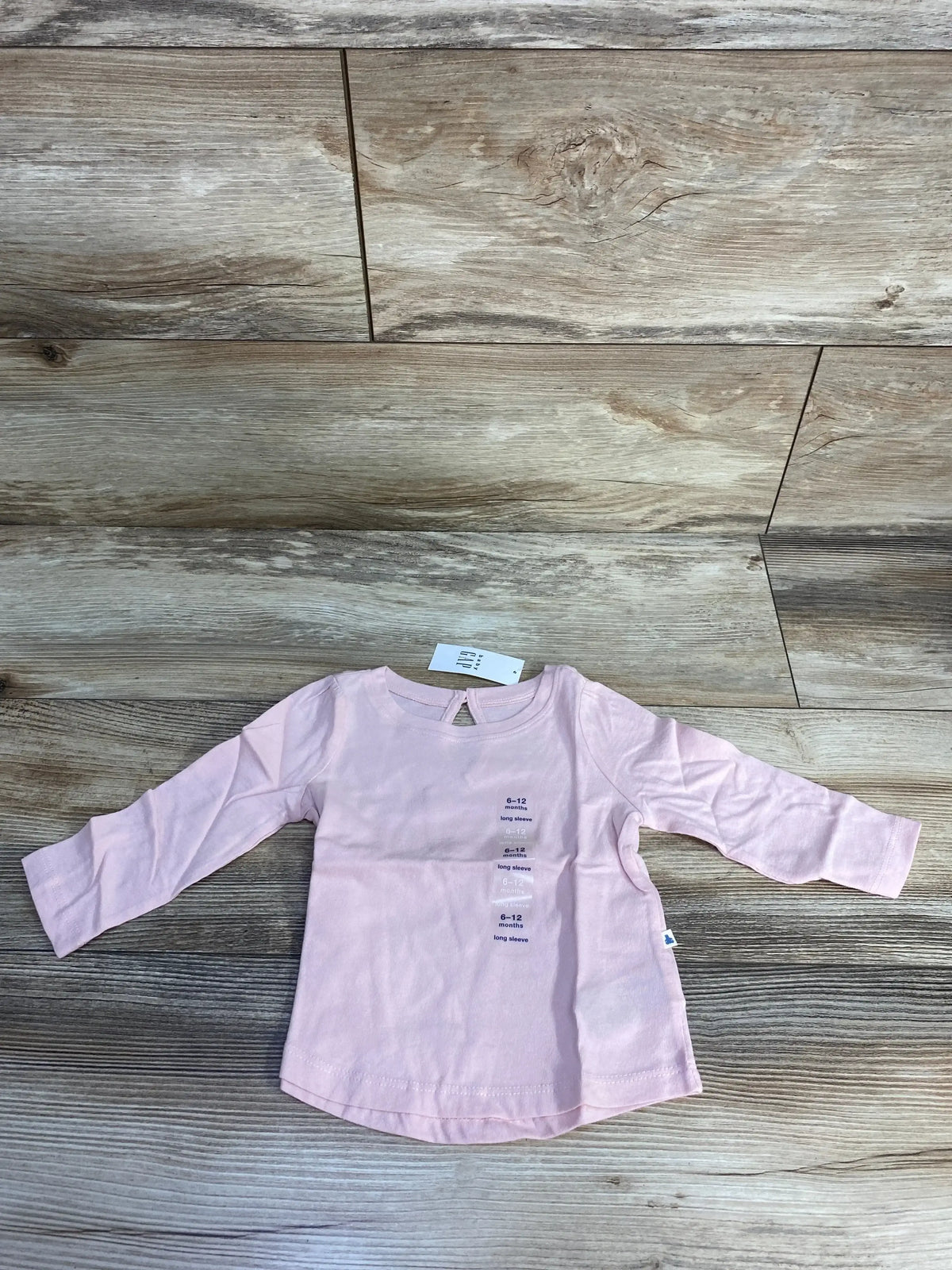 Light pink long sleeve baby shirt size 6-12 months on wood floor