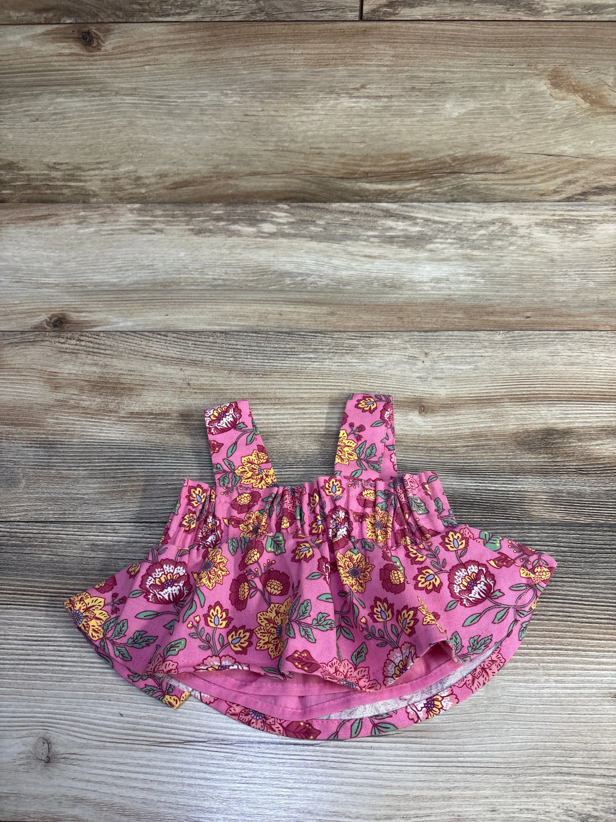 Top-down view of pink floral smocked cropped baby tank top (size 12 months) showing smocked bodice and ruffled hem on wood background