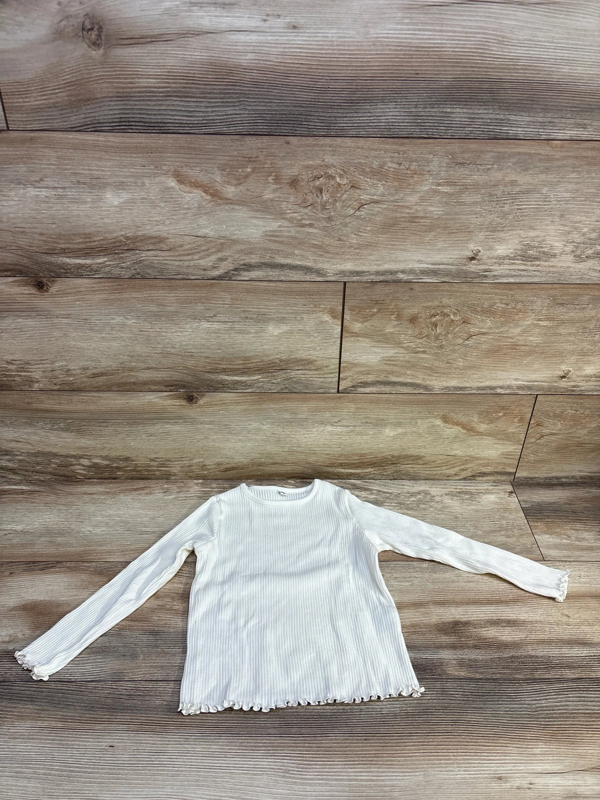 Flat lay of Uniqlo ivory ribbed long-sleeve shirt (4/5T) showing ribbed fabric and lettuce-edge hem on wood floor