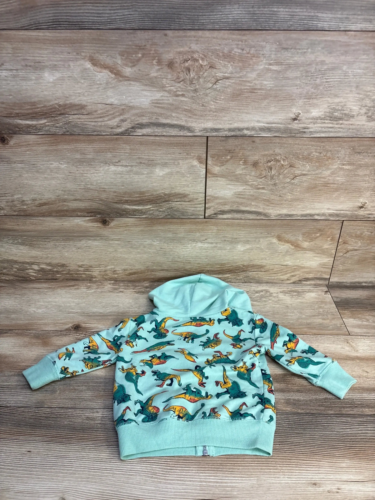 Mint green toddler hoodie with colorful dinosaur print, laid on wood floor