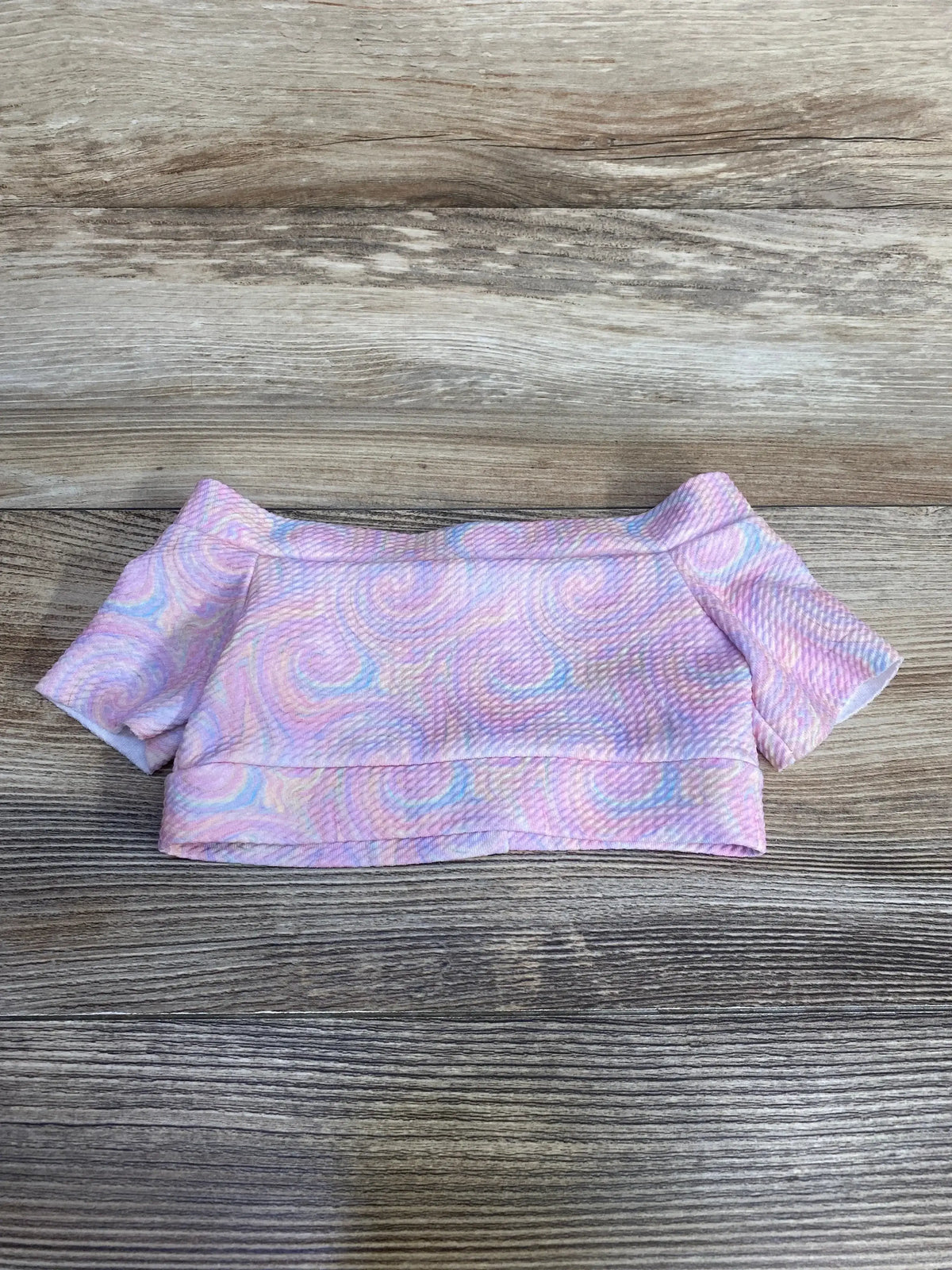 Flat lay of pink baby cropped top for 3 to 6 months showcasing short sleeves and pastel swirl textured fabric on wood background