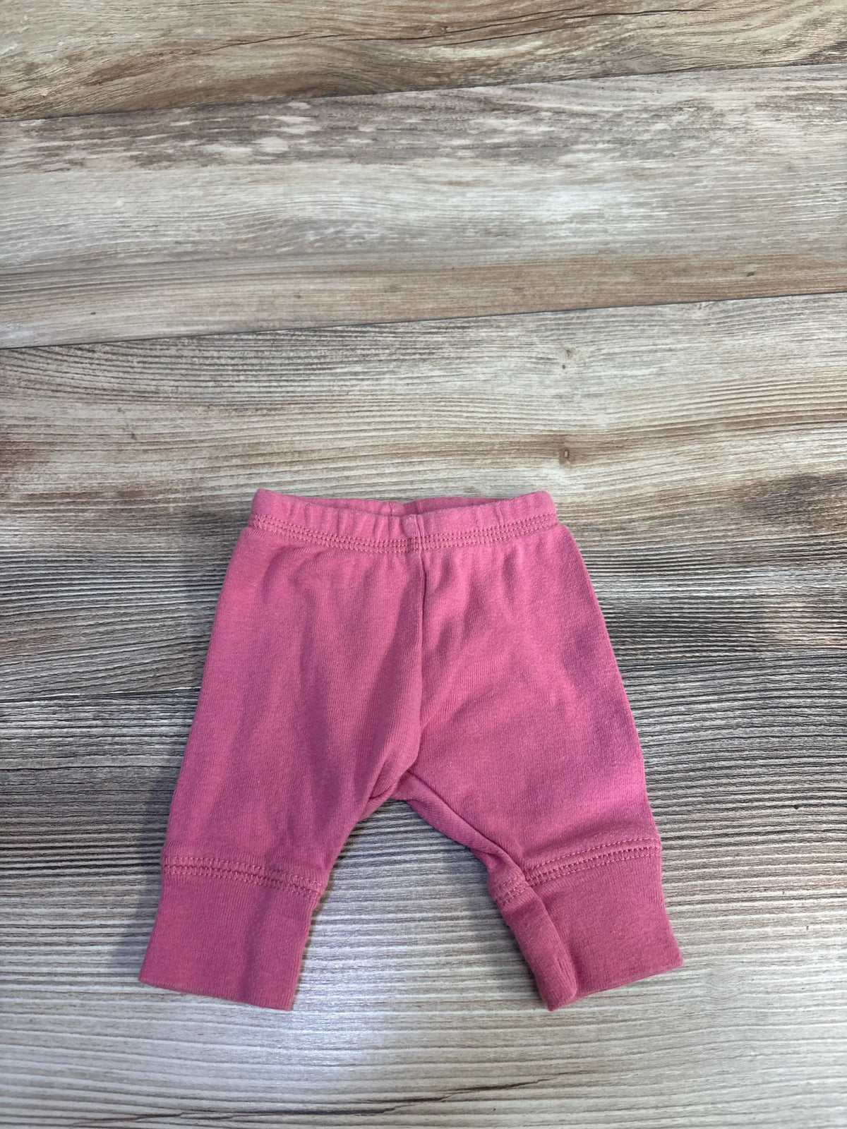 Front view of Simple Joys pink preemie pants showcasing elastic waistband and ribbed cuffs on a wood-look background