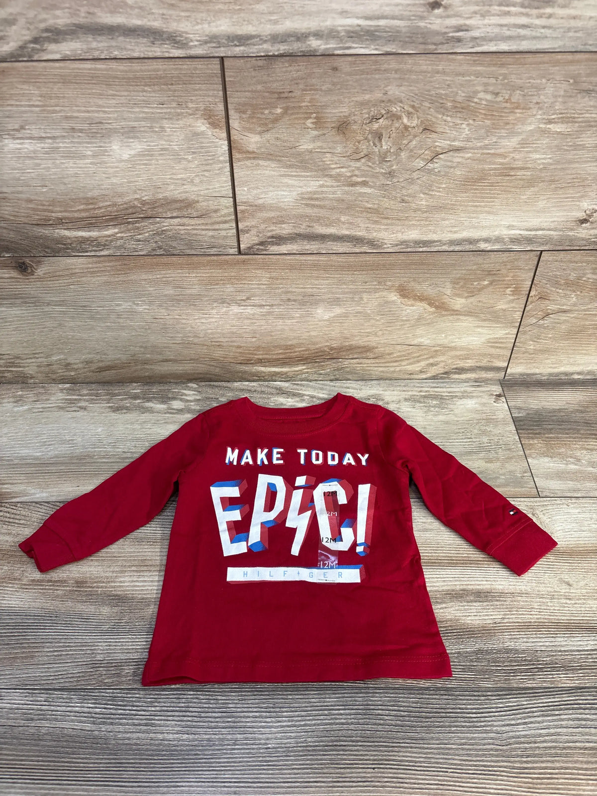 Front view of a red Tommy Hilfiger shirt in size 12 months showcasing the Make Today Epic graphic on a wood floor