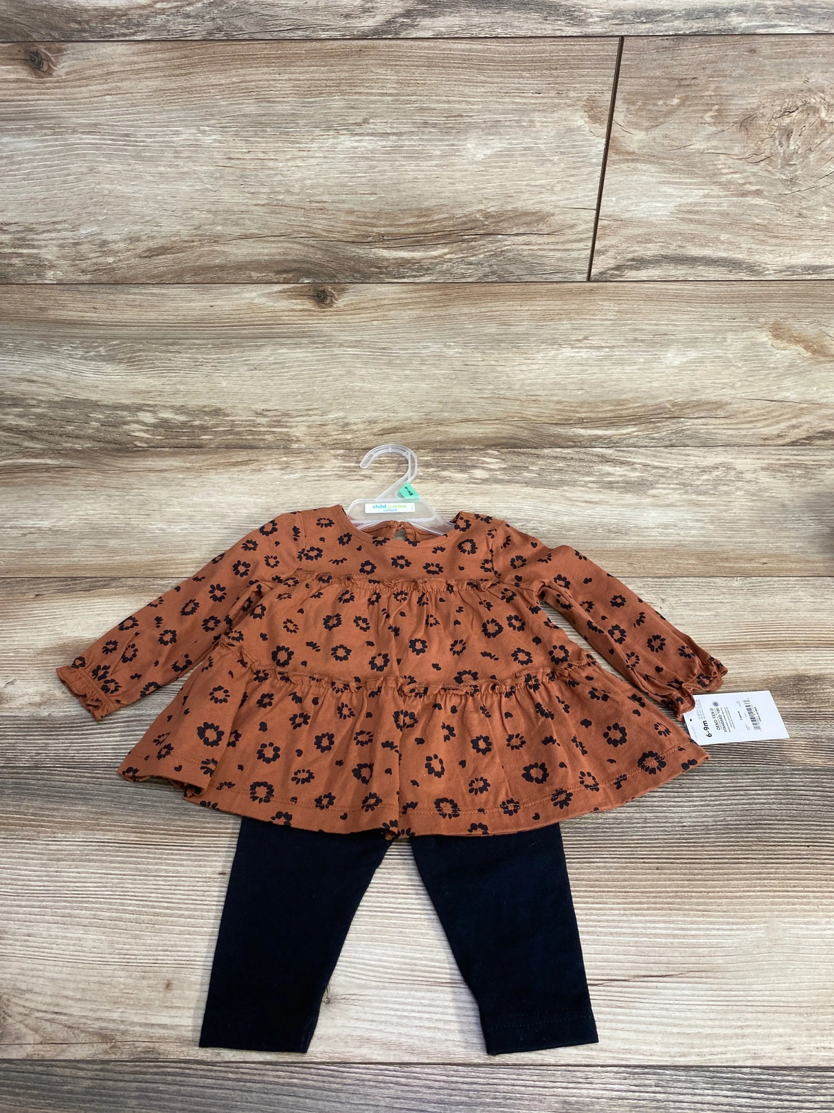 Flat lay of Child Of Mine 2-piece brown floral long-sleeve dress with ruffled tiers and black leggings on wood floor