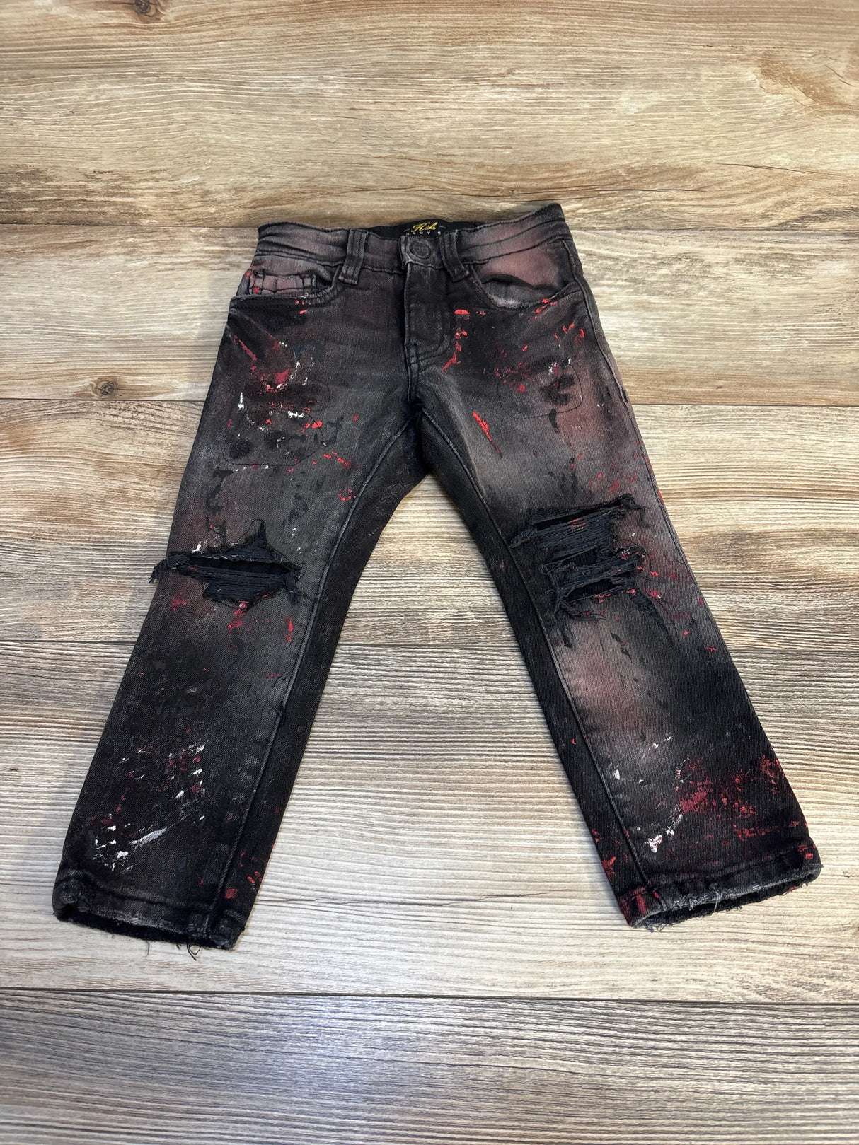 Distressed black kids jeans with paint splatter and ripped knees on wood background