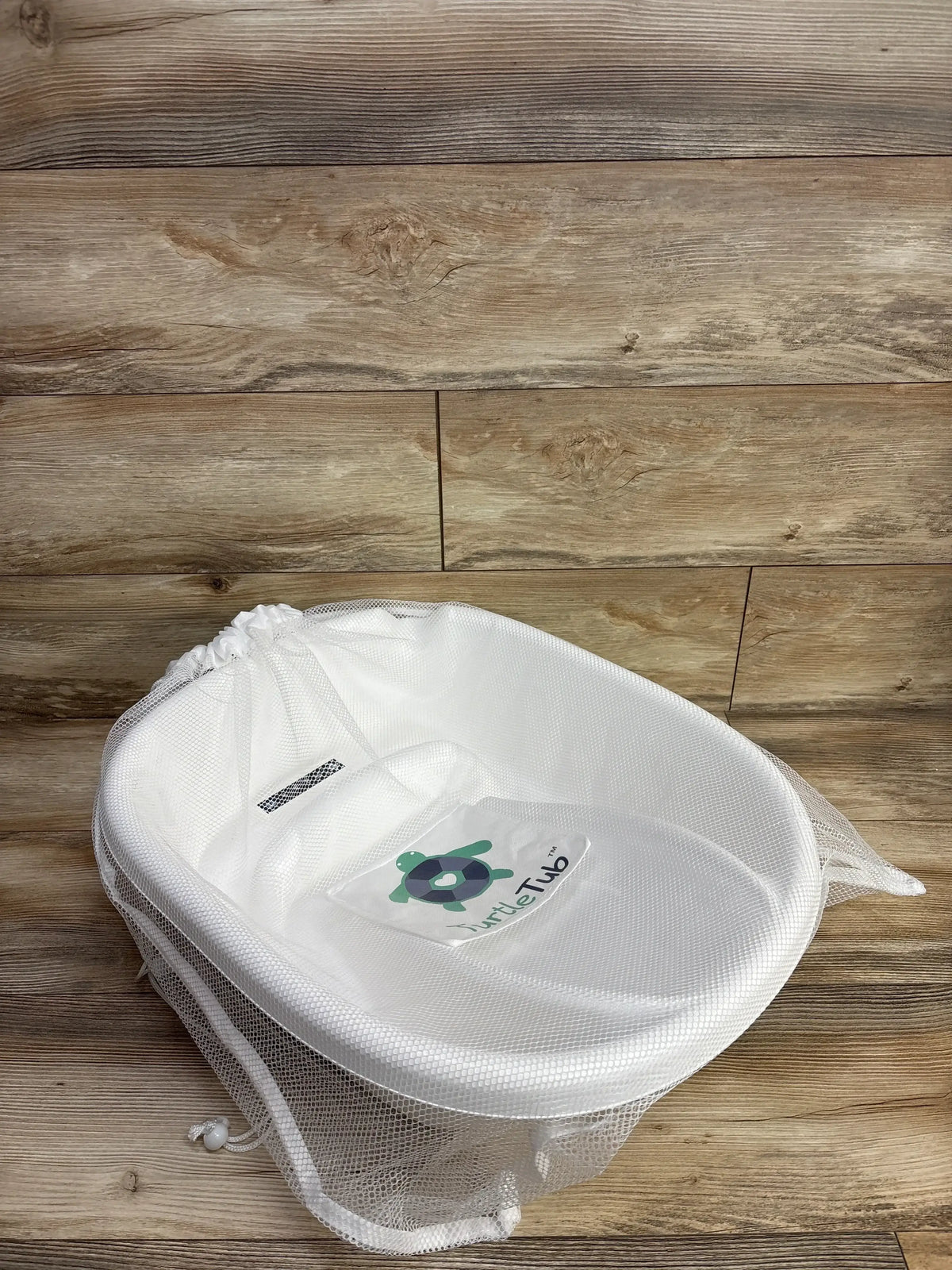 Angled top-down view of TurtleTub Swaddle Bath Tub showing white mesh fabric, contoured seat and TurtleTub logo on wood floor